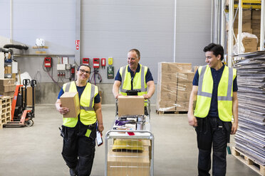 Smiling multi-ethnic coworkers walking with cart at distribution warehouse - MASF09143