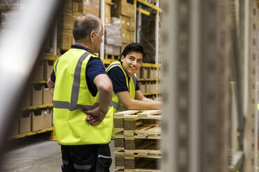 Smiling young worker looking at senior coworker standing at distribution warehouse - MASF09156