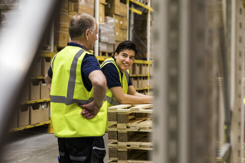 Lächelnder junger Arbeiter, der einen älteren Kollegen in einem Vertriebslager ansieht - MASF09156