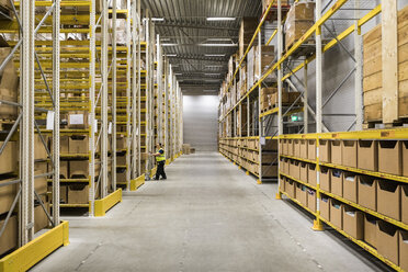 Full length of mature female warehouse worker pushing cart on aisle in industrial building - MASF09163