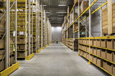 Aisle amidst packages on racks at illuminated distribution warehouse - MASF09165