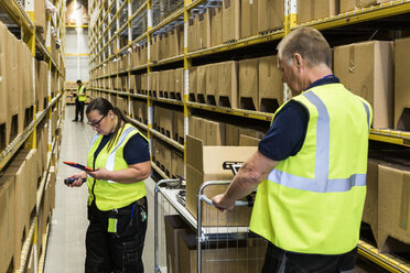 Coworkers working on aisle amidst racks at distribution warehouse - MASF09172