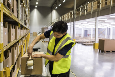 Young male worker packing cardboard box with adhesive tape at distribution warehouse - MASF09179