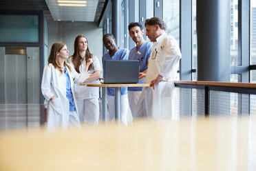 Confident healthcare workers discussing over laptop on table in corridor at hospital - MASF09192