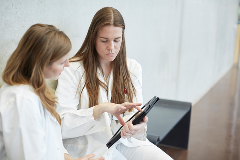 Selbstbewusste Ärztinnen diskutieren über ein digitales Tablet, während sie auf dem Flur eines Krankenhauses sitzen, lizenzfreies Stockfoto