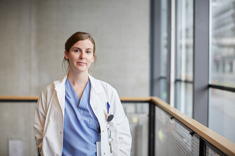 Porträt einer zuversichtlichen Ärztin im mittleren Erwachsenenalter am Fenster im Korridor eines Krankenhauses, lizenzfreies Stockfoto