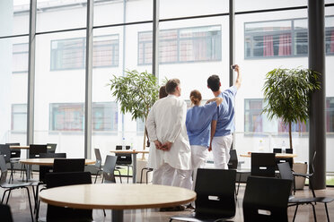 Rückansicht eines Krankenpflegers, der ein Selfie mit dem medizinischen Team in der Cafeteria eines Krankenhauses macht - MASF09218