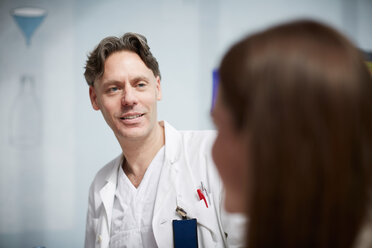 Smiling mature doctor looking at female coworker while sitting in hospital cafeteria - MASF09229