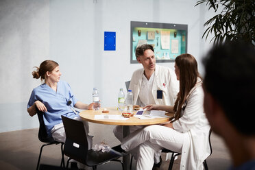 Selbstbewusster reifer Arzt im Gespräch mit weiblichen Kollegen am Tisch in der Krankenhaus-Cafeteria - MASF09230