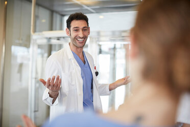 Cheerful young male doctor gesturing to female nurse while standing in lobby at hospital - MASF09262