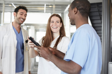 Lächelndes multiethnisches Gesundheitspersonal diskutiert über ein digitales Tablet, während es in der Lobby eines Krankenhauses steht - MASF09272
