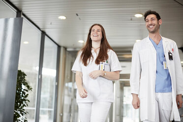 Lächelndes junges Gesundheitspersonal schaut weg, während es in der Lobby eines Krankenhauses geht - MASF09273