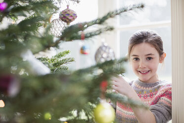 Porträt lächelndes Mädchen beim Schmücken des Weihnachtsbaums - HOXF03769