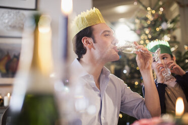 Daughter watching happy father in paper crown drinking champagne at Christmas dinner - HOXF03770