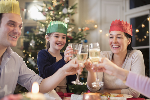 Glückliche Familie in Papierkrähen, die beim Weihnachtsessen mit Wasser und Sekt anstoßen, lizenzfreies Stockfoto