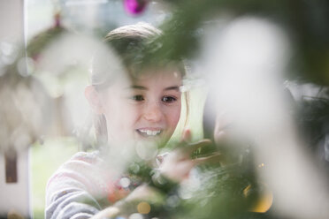 Lächelndes Mädchen beim Schmücken des Weihnachtsbaums - HOXF03776