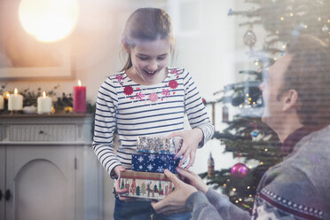 Tochter übergibt ihrem Vater im Wohnzimmer einen Stapel Weihnachtsgeschenke - HOXF03777
