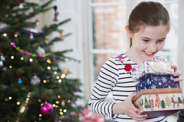 Lächelndes, eifriges Mädchen, das im Wohnzimmer Weihnachtsgeschenke sammelt - HOXF03780