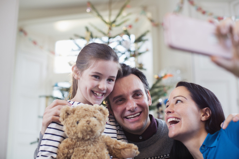 Glückliche Eltern und Tochter machen ein Selfie vor dem Weihnachtsbaum, lizenzfreies Stockfoto