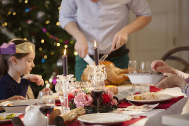 Vater tranchiert Weihnachtstruthahn bei Kerzenlicht am Tisch - HOXF03793