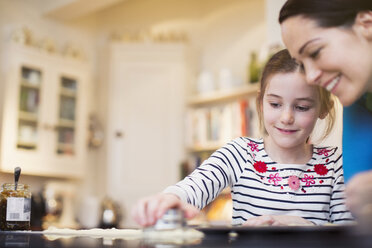 Mother and daughter baking, using cookie cutter in kitchen - HOXF03796