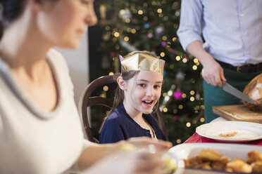 Lächelndes Mädchen mit Papierkrone beim Weihnachtsessen - HOXF03797