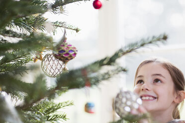 Smiling girl looking up at ornaments on Christmas tree - HOXF03802