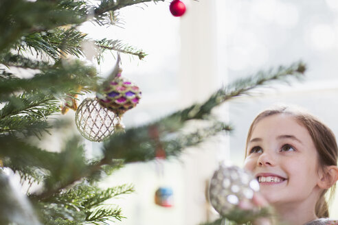 Lächelndes Mädchen mit Blick auf den Schmuck am Weihnachtsbaum - HOXF03802