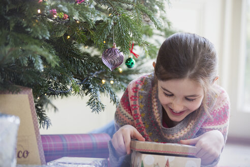 Lächelndes, neugieriges Mädchen öffnet Weihnachtsgeschenk - HOXF03805