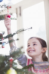 Smiling, curious girl touching ornament on Christmas tree - HOXF03811