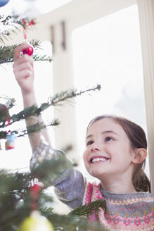Lächelndes, neugieriges Mädchen, das ein Ornament am Weihnachtsbaum berührt - HOXF03811