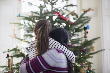 Zärtliche Mutter und Tochter umarmen sich vor dem Weihnachtsbaum - HOXF03813