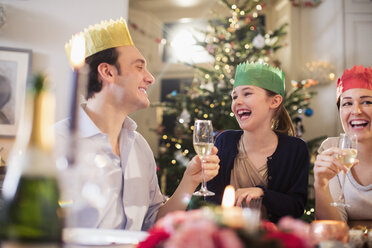 Eine glückliche Familie in Papierkronen genießt das Weihnachtsessen, trinkt Champagner und lacht - HOXF03818
