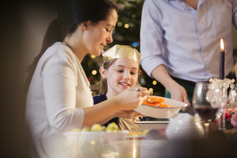 Mutter serviert ihrer Tochter beim Weihnachtsessen Karotten in einer Papierkrone, lizenzfreies Stockfoto