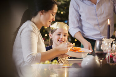 Mutter serviert ihrer Tochter beim Weihnachtsessen Karotten in einer Papierkrone - HOXF03820