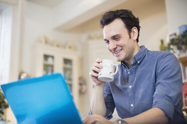 Lächelnder Mann trinkt Kaffee und arbeitet am Laptop - HOXF03823