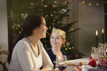 Glückliche Mutter und Tochter in Papierkrone bei Kerzenschein Weihnachtsessen Tisch - HOXF03837