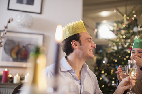 Glücklicher Vater und Tochter in Papierkronen trinken Wasser und Champagner beim Weihnachtsessen bei Kerzenschein - HOXF03841