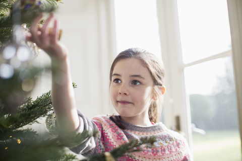 Neugieriges Mädchen berührt das Ornament am Weihnachtsbaum, lizenzfreies Stockfoto