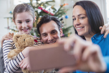 Glückliche Familie mit Smartphone, die ein Selfie im Weihnachtswohnzimmer macht - HOXF03860