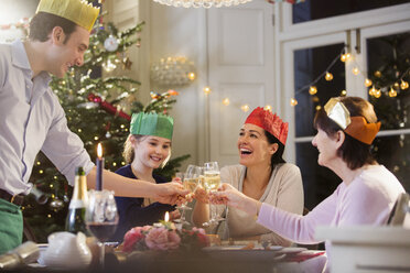 Mehrgenerationenfamilie in Papierkronen stößt beim Weihnachtsessen bei Kerzenschein mit Champagnerflöten an - HOXF03867