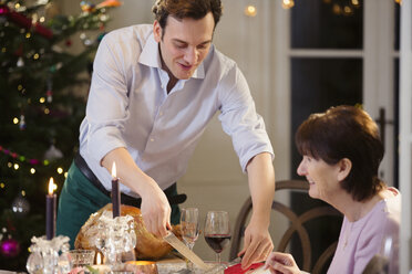 Sohn serviert seiner älteren Mutter bei Kerzenlicht den Weihnachtstruthahn - HOXF03869