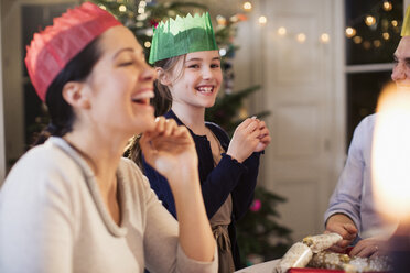 Glückliche Familie in Papierkronen lacht beim Weihnachtsessen - HOXF03876