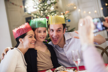 Verspielte Familie mit Papierkronen posiert für ein Foto am Weihnachtstisch - HOXF03878