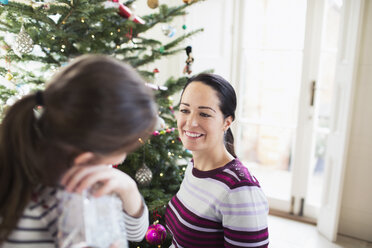 Lächelnde Mutter und Tochter im Gespräch am Weihnachtsbaum - HOXF03880