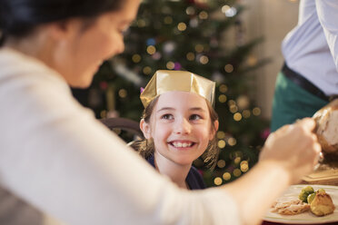 Lächelndes Mädchen mit Papierkrone genießt das Weihnachtsessen - HOXF03882