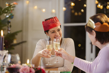 Tochter und ältere Mutter mit Papierkronen stoßen am Weihnachtstisch mit Sektgläsern an - HOXF03884