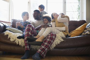 Young family relaxing in pajamas on living room sofa - HOXF03890