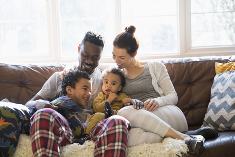 Multiethnische junge Familie entspannt sich im Schlafanzug auf dem Wohnzimmersofa, lizenzfreies Stockfoto