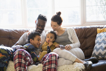 Multi-ethnic young family relaxing in pajamas on living room sofa - HOXF03896